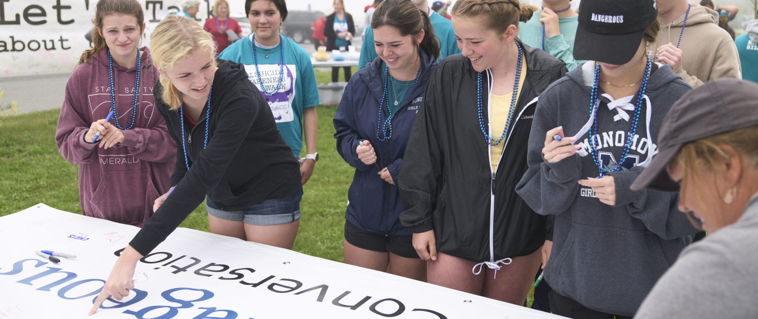 A group of teenagers surrounding and pointing at a sign at the Cape & Islands Suicide Awareness Walk